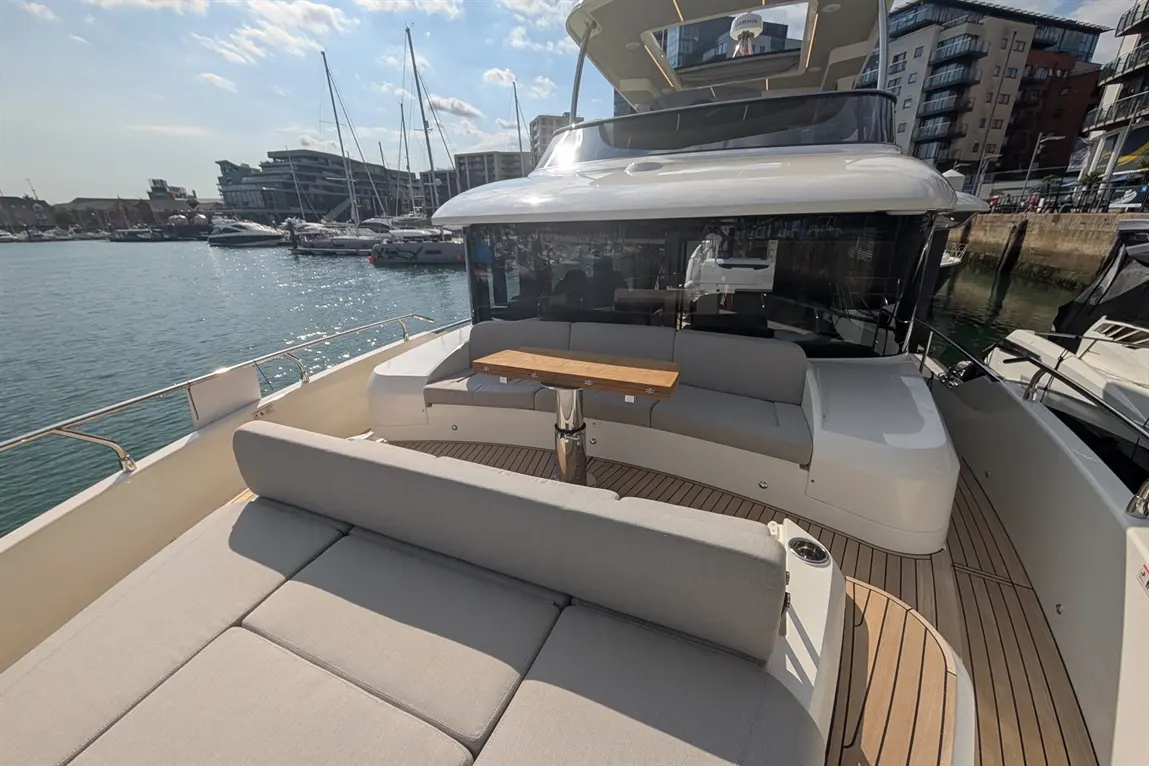Luxury yacht deck featuring grey cushions, a wooden table, and scenic views of the marina and buildings.